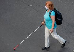 Frau überquert mit Hilfe eines Blindenstockes eine Straße