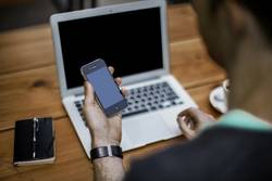 Ein Mann sitzt am Laptop und blickt gleichzeitig auf sein Smartphone (Symbolfoto).