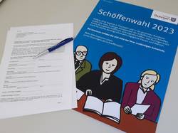 Der Bewerbungsbogen für die Jugendschöffenwahl im Saale-Orla-Kreis liegt neben dem blauen Plakat des Thüringer Justizministeriums zur Schöffenwahl 2023 auf einem Tisch (Symbolfoto).