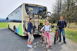 Eine Gruppe steht hinter einem Bus mit Fahrradgepäckträger (Symbolfoto)