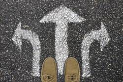 Zwei Füße stehen an drei Richtungspfeilen auf einer Straße (Symbolfoto).