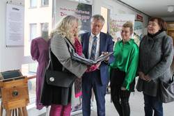 Gemeinsam mit Monika Wohlfahrt (von links), Ida Knoll und Gabriela Seidel vom Handels- und Gewerbeverein Schleiz betrachtet Landrat Thomas Fügmann eine Sammlung zur Schleizer Modenacht, die die Ausstellung begleitet.