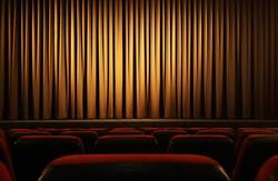 Blick über mehrere Stuhlreihen hinweg auf den geschlossenen Vorhang eines Kinosaals (Symbolfoto).