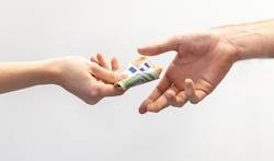 Eine Hand reicht einer anderen Hand mehrere Geldscheine (Symbolfoto).