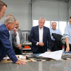 Im Beisein seiner Söhne Mathias und Steve erklärt Geschäftsführer und Inhaber Steffen Weiser (von rechts) der Delegation um Landrat Thomas Fügmann anhand der Baupläne eines der aktuellen Projekte des Unternehmens.