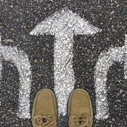 Zwei Füße stehen an drei Richtungspfeilen auf einer Straße (Symbolfoto).