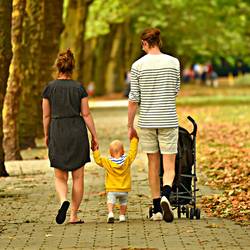Eine Familie mit Kinderwagen spaziert durch einen Park (Symbolfoto)