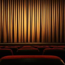 Blick über mehrere Stuhlreihen hinweg auf den geschlossenen Vorhang eines Kinosaals (Symbolfoto).