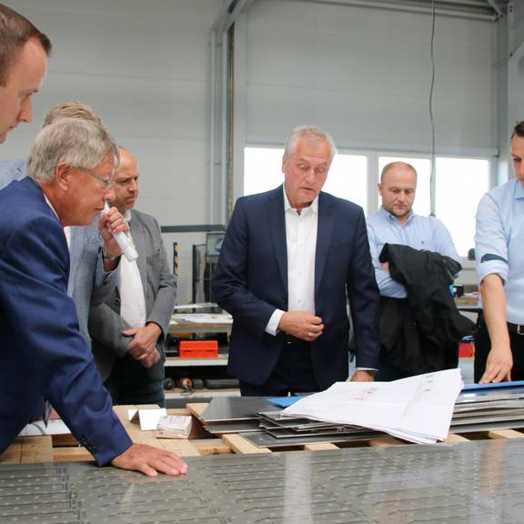 Im Beisein seiner Söhne Mathias und Steve erklärt Geschäftsführer und Inhaber Steffen Weiser (von rechts) der Delegation um Landrat Thomas Fügmann anhand der Baupläne eines der aktuellen Projekte des Unternehmens.