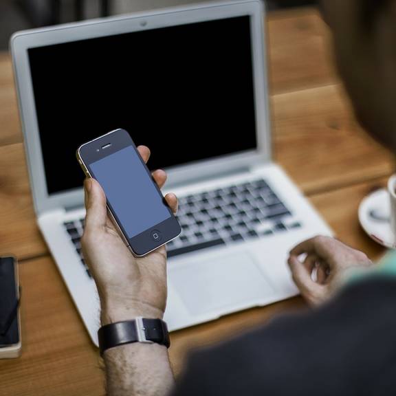 Ein Mann sitzt am Laptop und blickt gleichzeitig auf sein Smartphone (Symbolfoto).