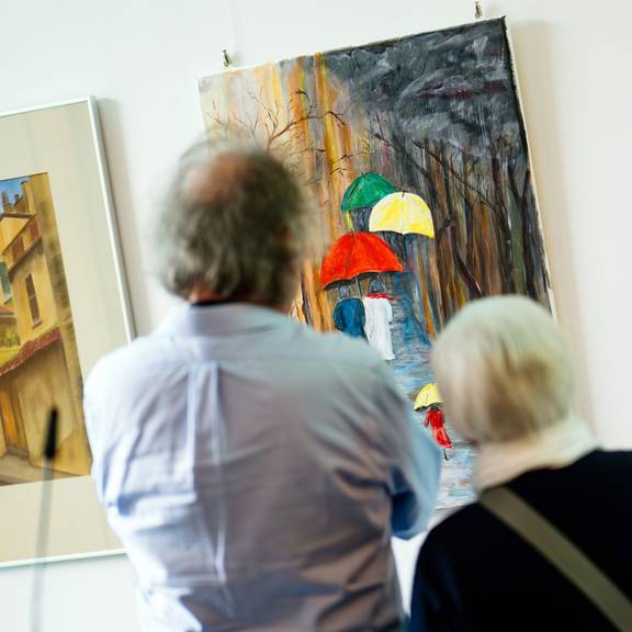 Zwei Personen betrachten eines der ausgestellten Bilder.